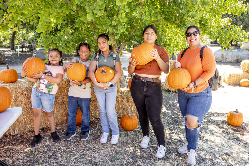 Family of five smiling and holding pumpkins at the pumpkin patch